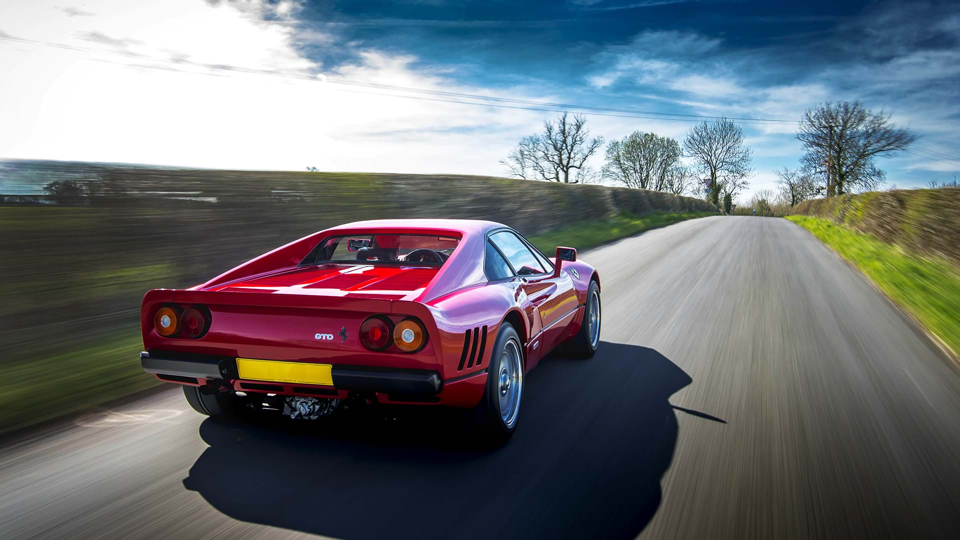 Ein klassischer roter Ferrari 288 GTO rastet eine malerische Landstraße entlang. 