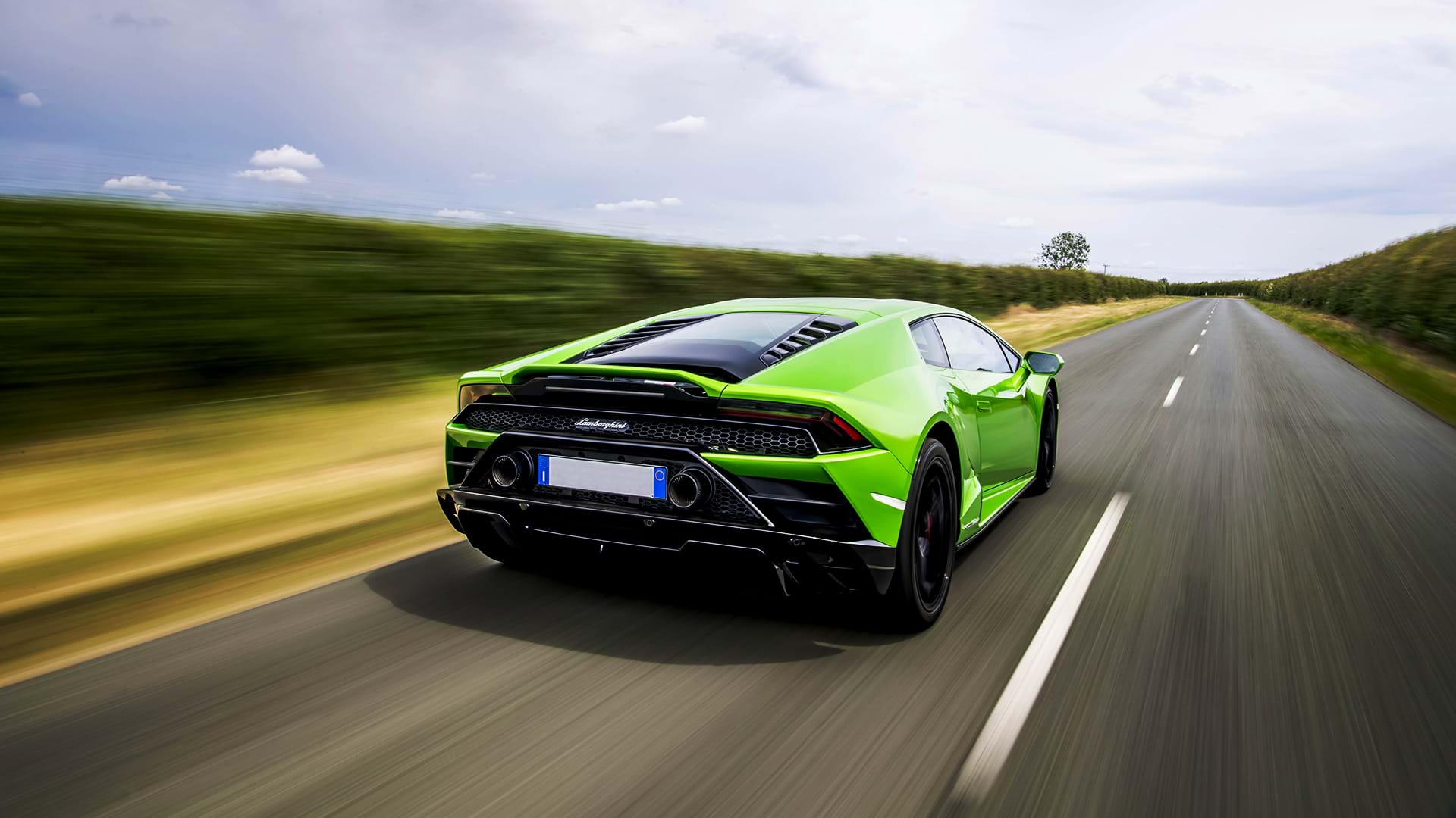 Leuchtend grüner Lamborghini Huracán Evo rastet an einem sonnigen Tag eine Landstraße entlang.