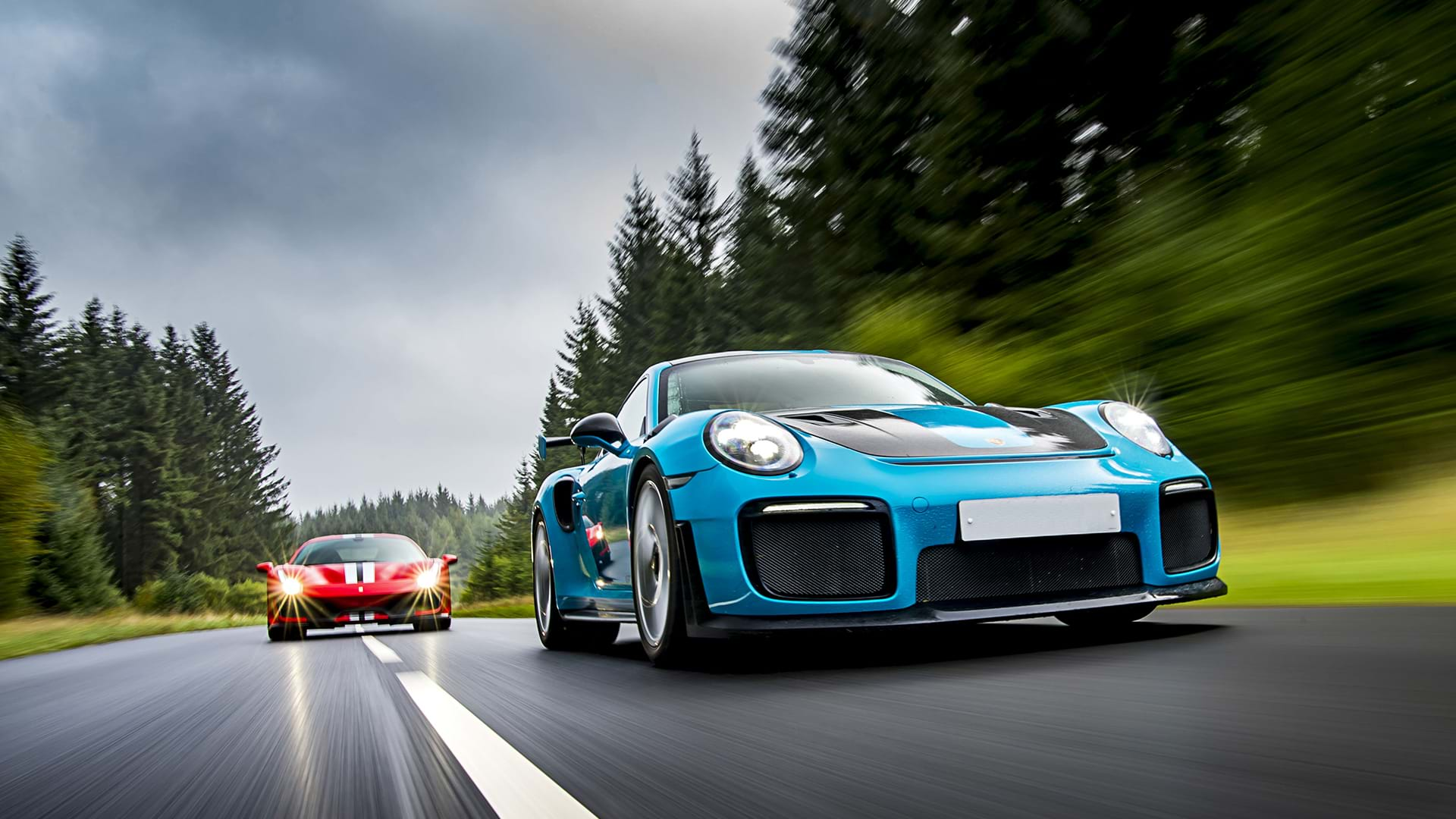 Blauer Porsche 991 GT3 RS führt zu einer roten Ferrari 488 Pista auf einer Panoramastraße. 