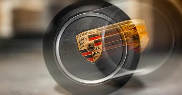 Porsche-Lenkradairbag mit detailliertem Porsche-Wappen in Nahaufnahme mit Bewegungsunschärfeeffekt.